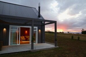 A modern house with a covered porch, a large sliding glass door leading to a living area, and a view of the sunset over a grassy field. - Beautiful Wairarapa views, short drive to all Martinborough has to offer (Martinborough)
