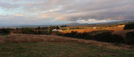 A rural landscape with rolling hills, a few scattered buildings, and a cloudy sky.