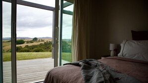 A bedroom with a large sliding glass door leading to a deck, a bed with a floral comforter, and a nightstand with a lamp. - Beautiful Wairarapa views, short drive to all Martinborough has to offer (Martinborough)