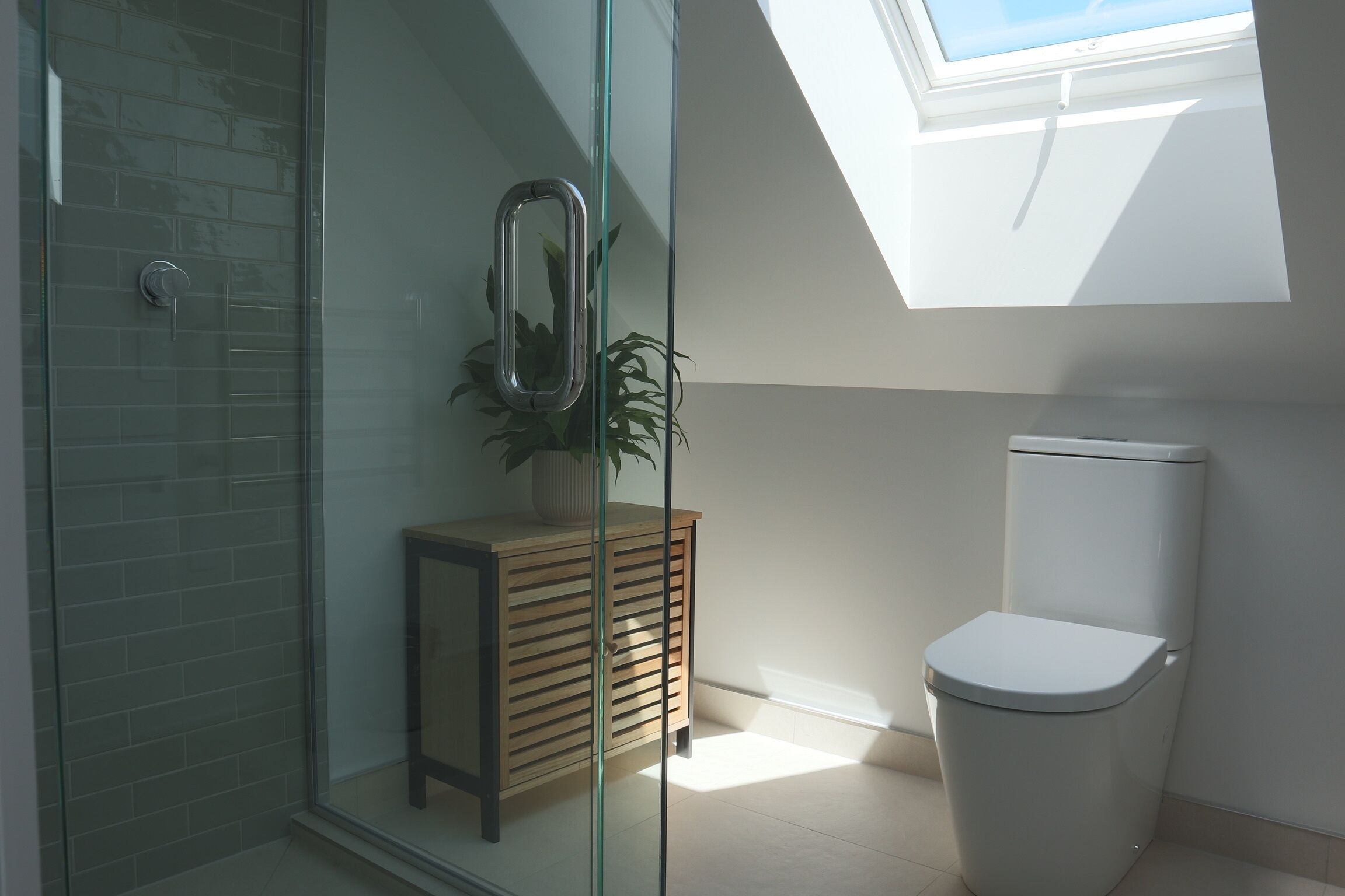 A modern bathroom with a glass shower enclosure, a wooden cabinet, a toilet, and a skylight.