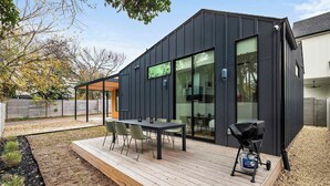 Ein modernes Haus mit Terrasse, Grill und überdachter Sitzgelegenheit im Freien.
