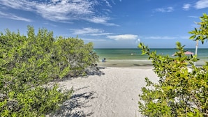 Une plage avec un ciel dégagé, un sentier sablonneux menant à l’eau et quelques zones verdoyantes.