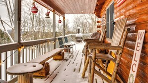 Una terraza de madera con un banco y un letrero de bienvenida, rodeada de árboles cubiertos de nieve.