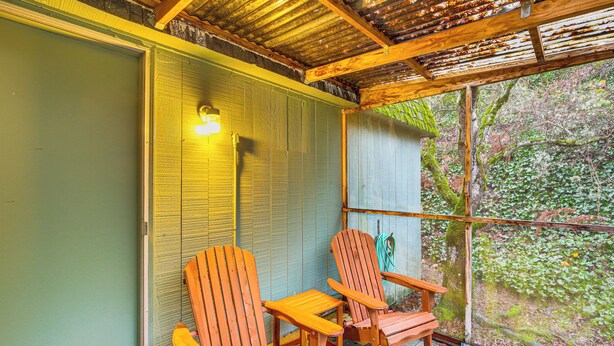 Une terrasse en bois avec deux fauteuils Adirondack et une porte vitrée donnant sur une zone boisée.