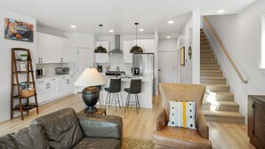 A modern kitchen with white cabinets, a central island, pendant lights, and a staircase leading to a loft bedroom. - Gateway to Yellowstone (Livingston)