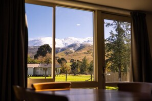 Una habitación con un ventanal que ofrece vistas a una montaña nevada, una cerca de madera y un edificio a lo lejos.