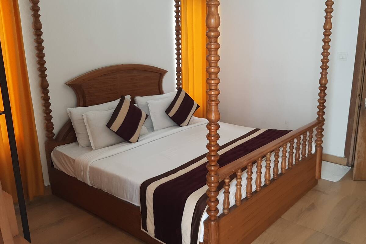 Una cama con dosel, cabecera de madera y colcha a rayas.