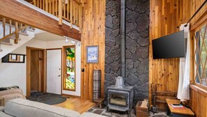 Una sala de estar acogedora con chimenea de piedra, paredes de madera, una escalera y un televisor de pantalla plana.