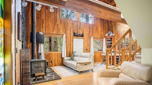 Interior acogedor de una cabaña con chimenea de piedra, paredes de madera, un sofá y una escalera.
