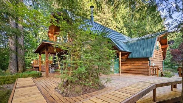Una cabaña de madera con techo metálico, rodeada de árboles.