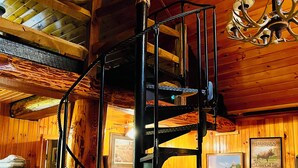 Een rustiek houten interieur met een spiltrap, houten wanden, een kroonluchter en een bed met sprei.