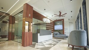 Un espace d’accueil moderne avec un mur en verre, des éléments décoratifs en bois, un canapé gris et un ventilateur de plafond.