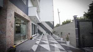 Un bâtiment moderne doté d’un sol à motifs géométriques, d’une entrée en verre et de plantes en pot disposées le long du chemin.