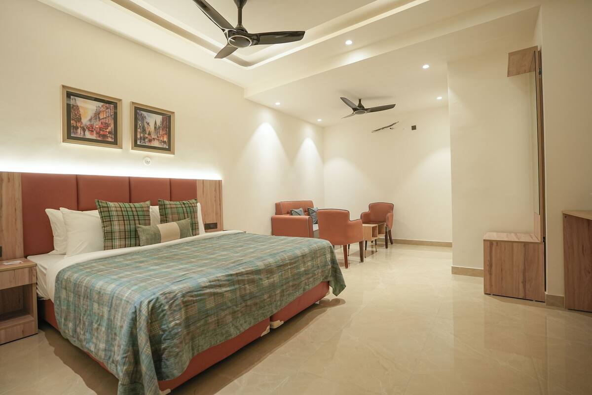 Une chambre d’hôtel moderne dotée d’un grand lit, de deux ventilateurs de plafond, d’un bureau avec une chaise et d’un petit coin salon.