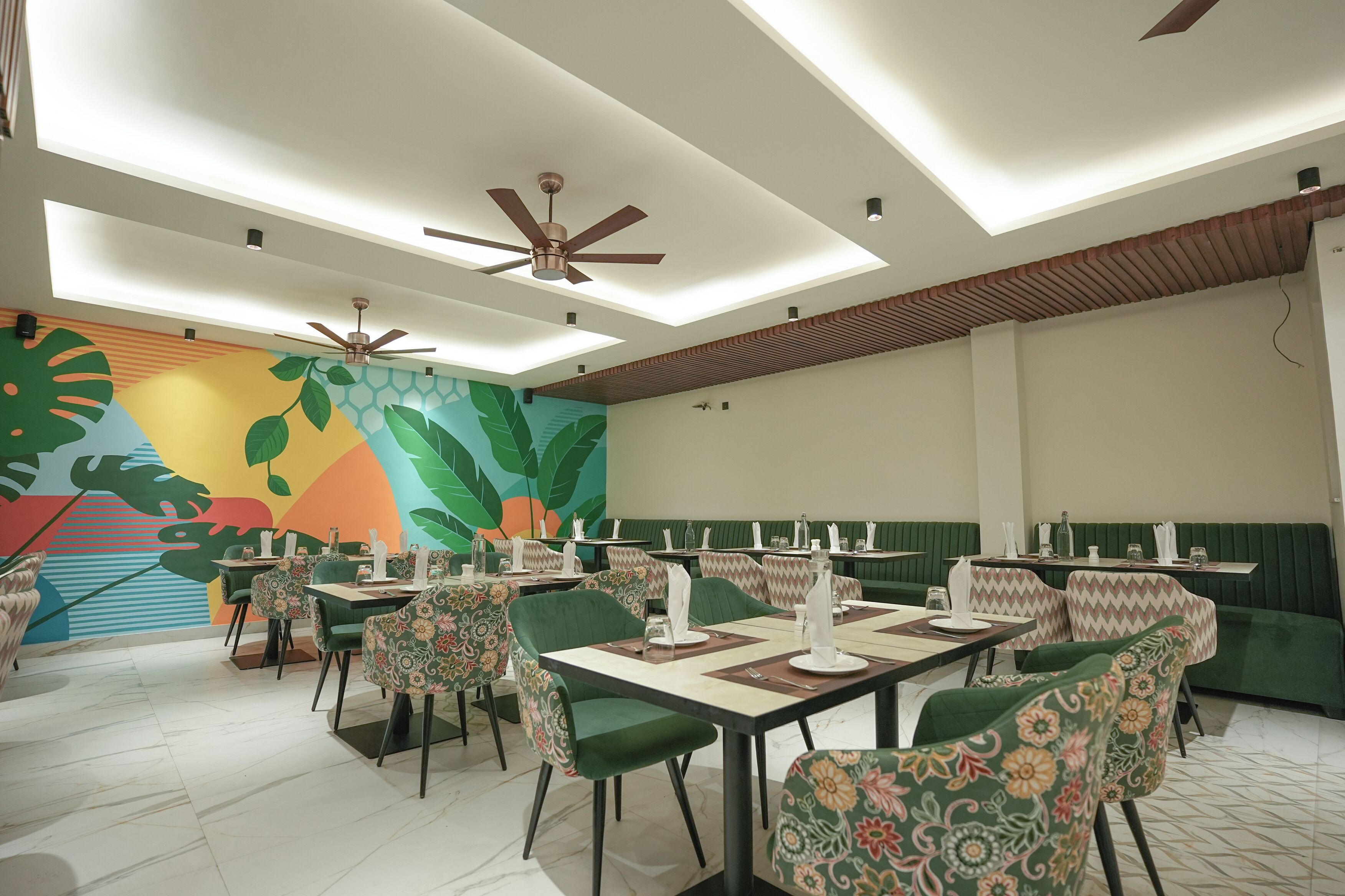 A restaurant with green booths and chairs, ceiling fans, and a colorful mural on the wall.