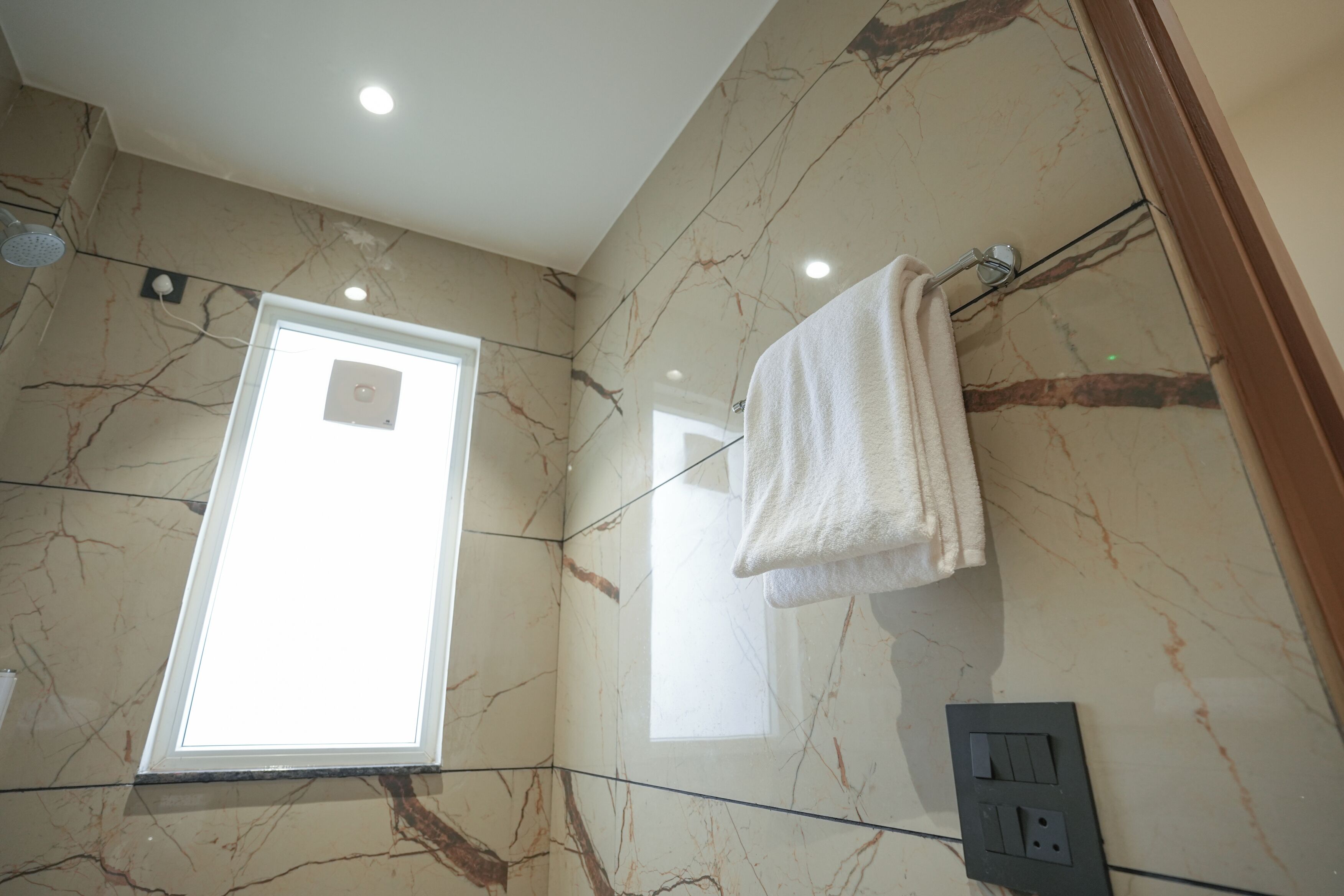 A bathroom with marble walls, a window, a towel rack, and a showerhead.