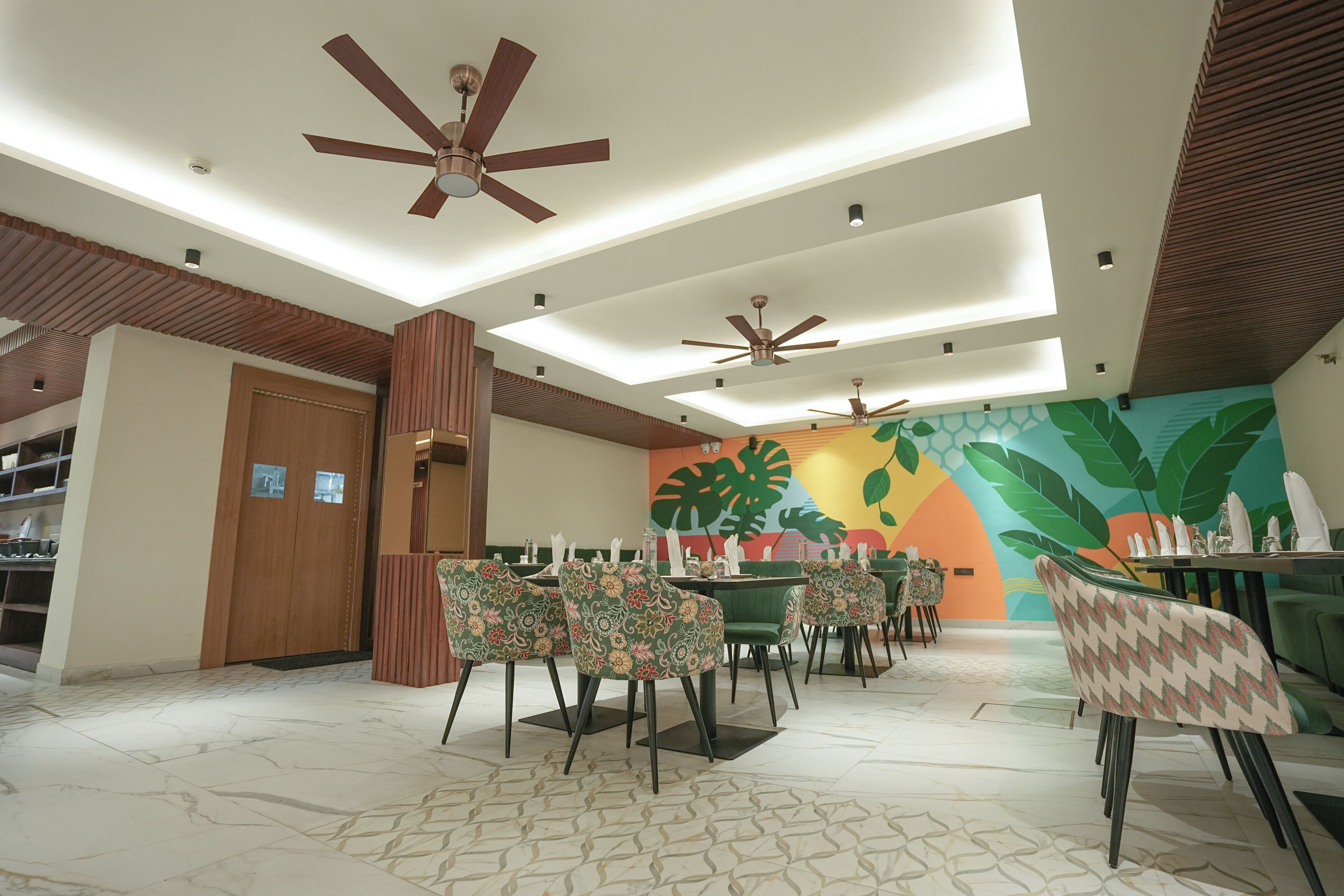 A restaurant with a modern ceiling design, multiple ceiling fans, and a vibrant mural on the wall.