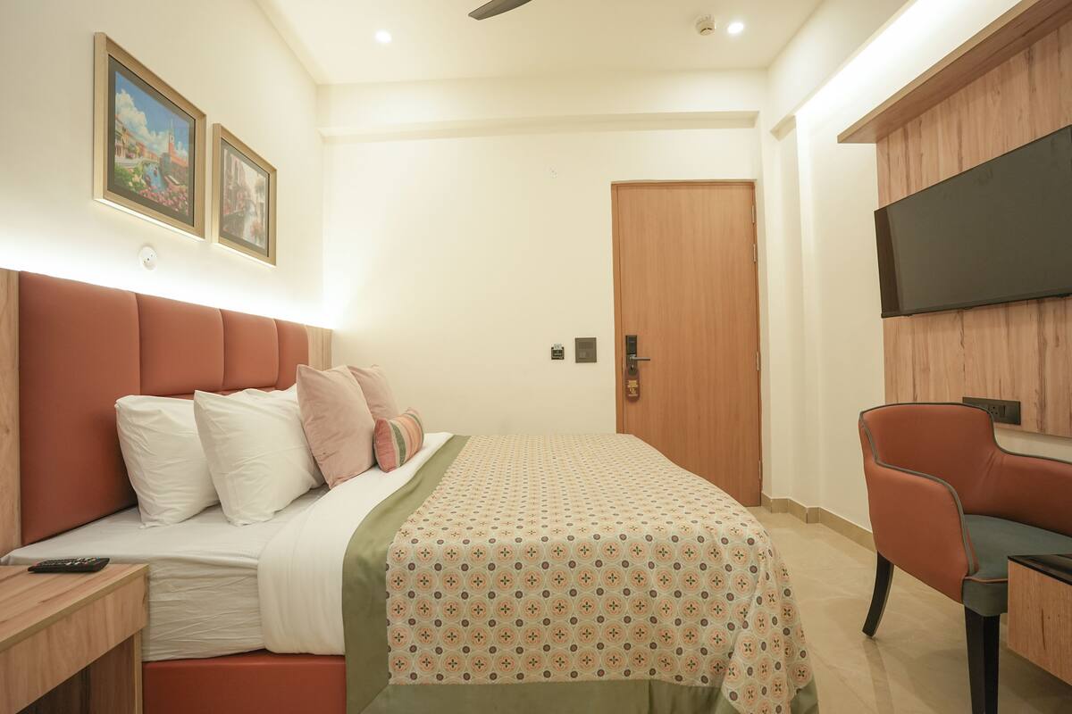 Une chambre bien rangée, avec un lit, une table de chevet et un téléviseur fixé au mur.