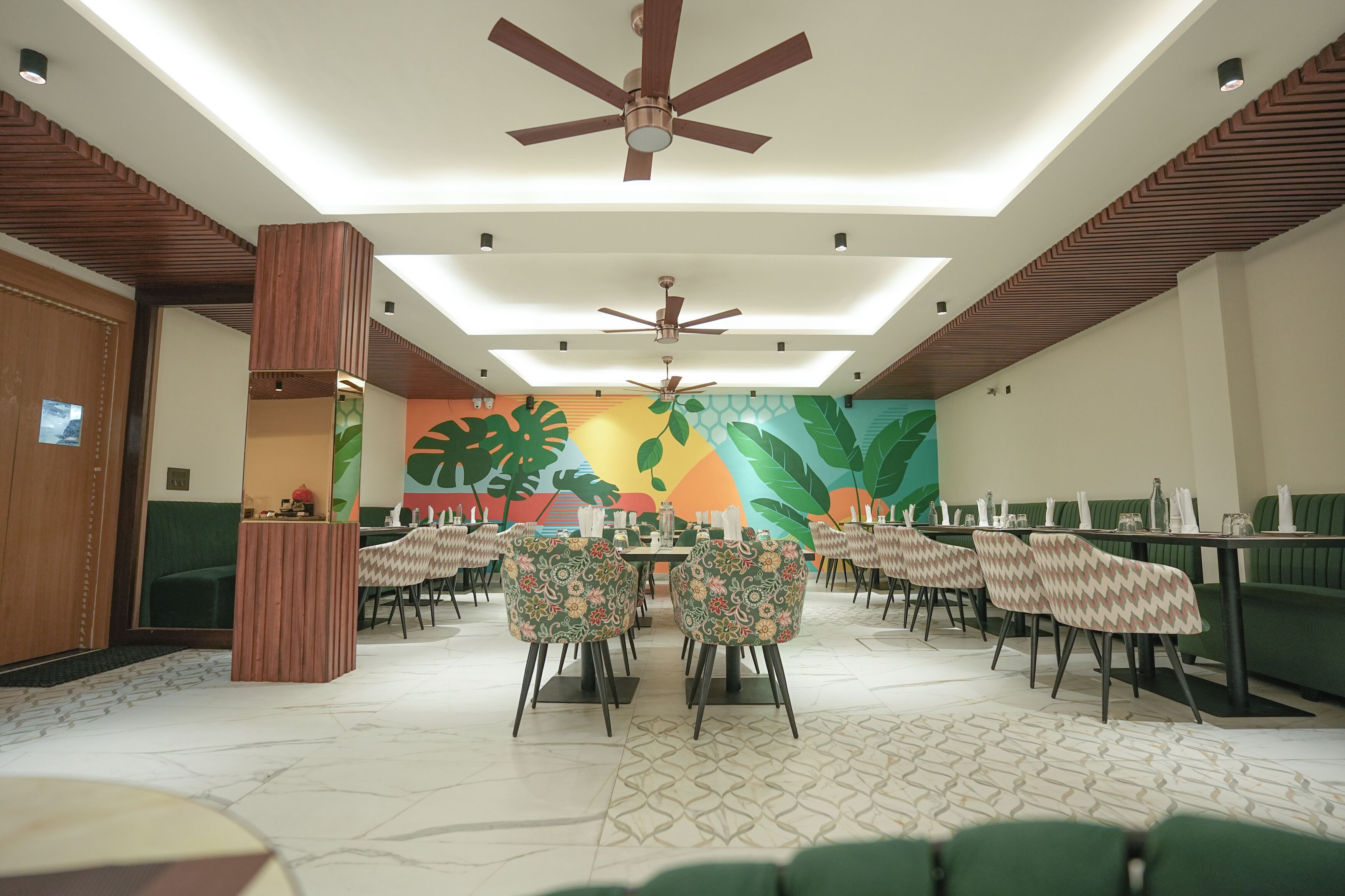 A restaurant with a central dining area, multiple ceiling fans, and a colorful mural on the back wall.