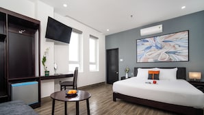 A hotel room with a bed, a desk, a chair, a small table with fruit, and a TV. - Coral Cove Hotel (Da Nang)