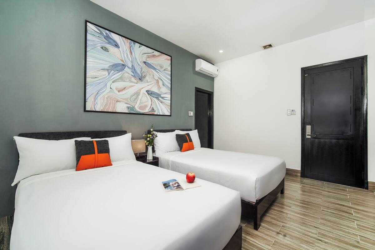 Een hotelkamer met twee bedden, een groot abstract schilderij, een airconditioning en een houten vloer.