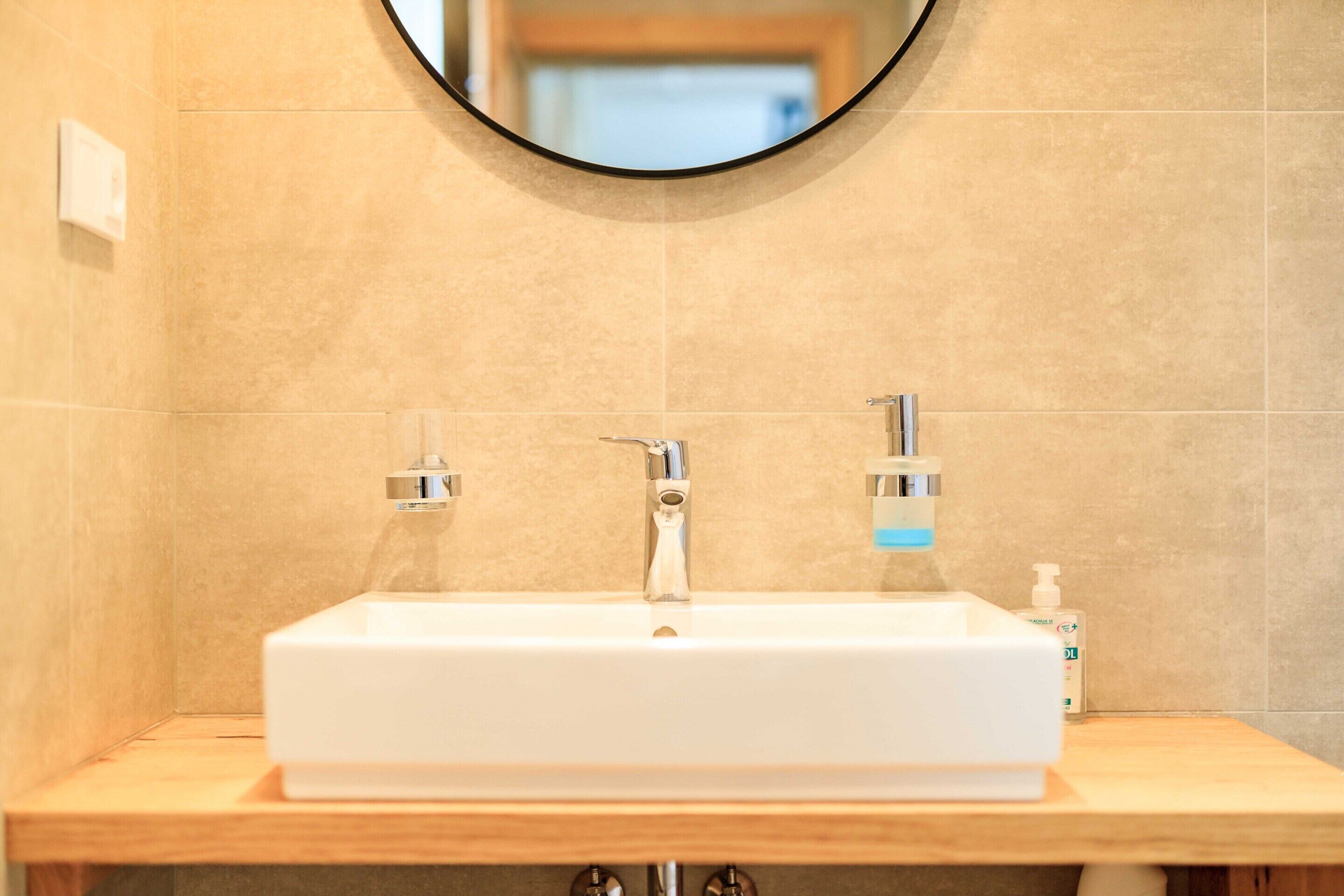 A bathroom with a rectangular sink, two faucets, a mirror above the sink, and a soap dispenser on the right.