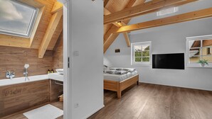 A modern bedroom with a skylight, wooden beams, a large window, a flat-screen TV, and a wooden bed. - Villa in Austria Near Ski Slopes & Sauna (Rokytnice nad Jizerou)