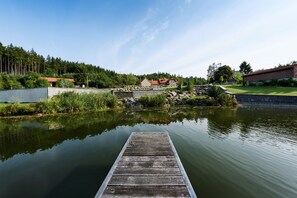 A wooden dock extending into a calm lake with a stone wall and greenery in the background. - Villa in Varvazov With Garden and Barbecue (Varvažov)