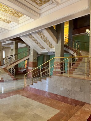 A grand staircase with marble steps and golden railings, leading to an upper level with ornate ceiling details. - Olive Garden Hotel Baku (Baku)