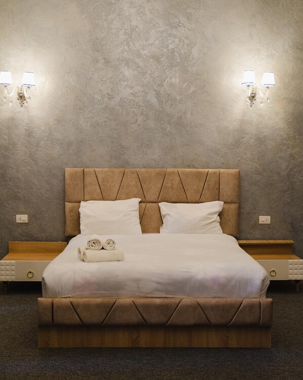 A bedroom with a large bed, two bedside tables, and wall-mounted light fixtures.