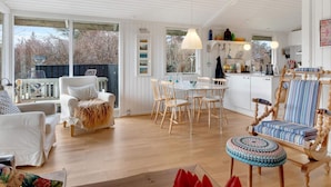 A spacious living area with a dining table, chairs, and a cozy seating area with a patterned ottoman. - 5 Star Holiday Home in Lokken (Lokken)