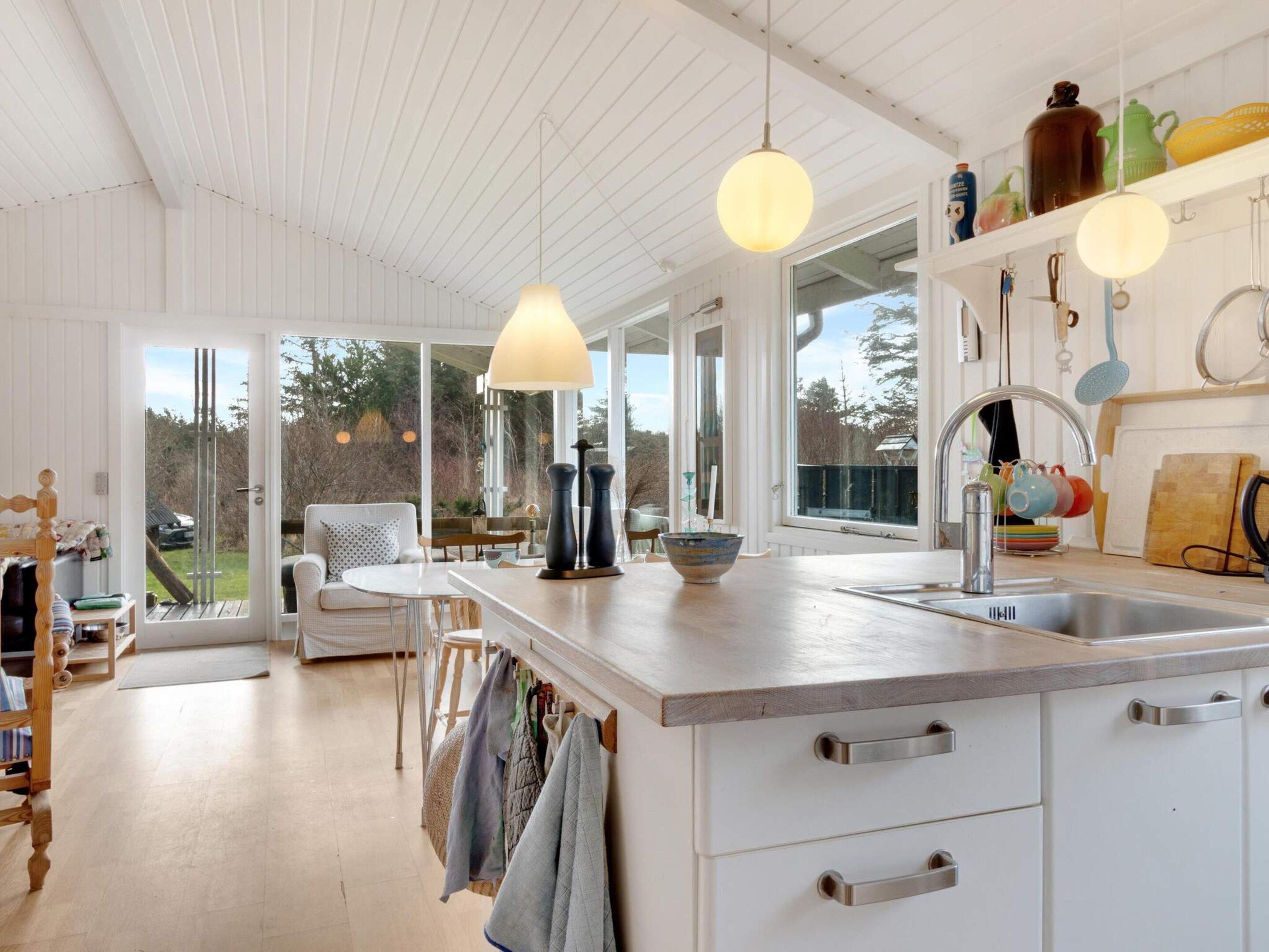 A modern kitchen with a large island, pendant lights, and a view of the outdoors.