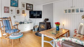 A cozy living room with a wooden floor, a sofa, a chair, a table, a fireplace, and various wall decorations. - 5 Star Holiday Home in Lokken (Lokken)