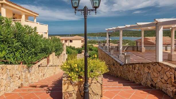 A stone pathway leading to a covered outdoor area with a view of the sea. - Delfino Apartment in Golfo Aranci (Golfo Aranci)