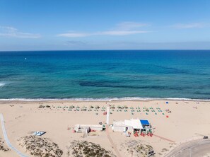 A beach with rows of sun loungers and umbrellas, a small building, and a clear view of the ocean.