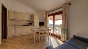 A compact kitchen with a dining area, a sofa, and a balcony with curtains. - Ancora Sardinia Seaside Apartment (Badesi)