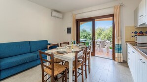 A dining area with a table set for four, a blue sofa, wooden chairs, and a view through a glass door to an outdoor patio. - Apartment Prua Sardinia Seaside (Badesi)