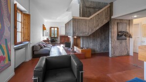 Un vaste espace de vie comprenant un canapé en cuir noir, un escalier en bois et un coin repas avec une table et des chaises.
