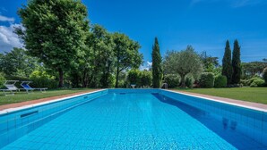 Une piscine d’un bleu éclatant, bordée de carreaux, entourée d’une pelouse et d’arbres.
