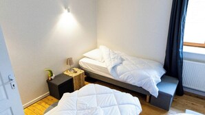 Une petite chambre à coucher moderne, avec deux lits, une table de chevet et une commode.