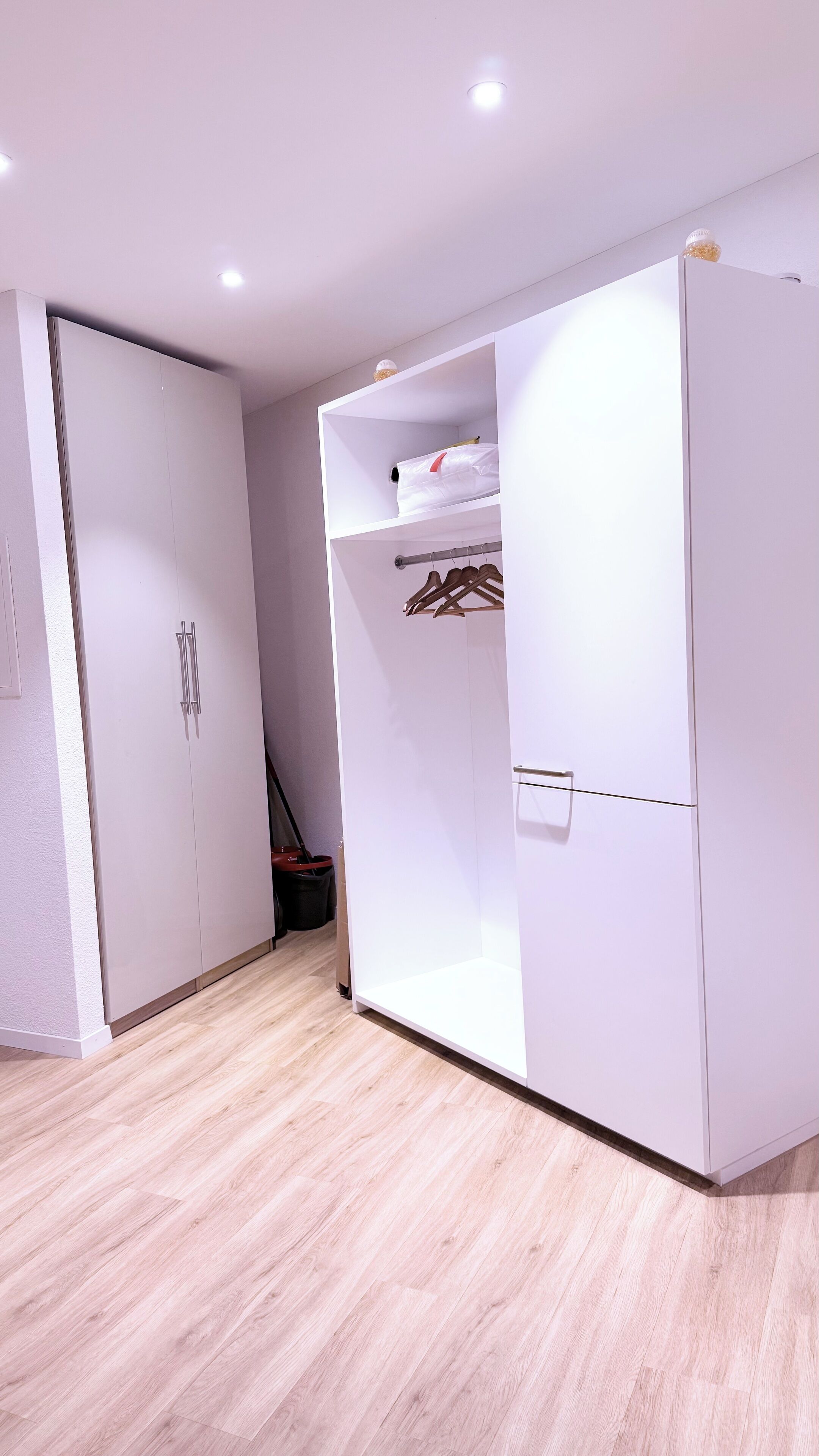 Een moderne, witte kamer met een kast, een schoenenrek en een klein plankje met een tas.