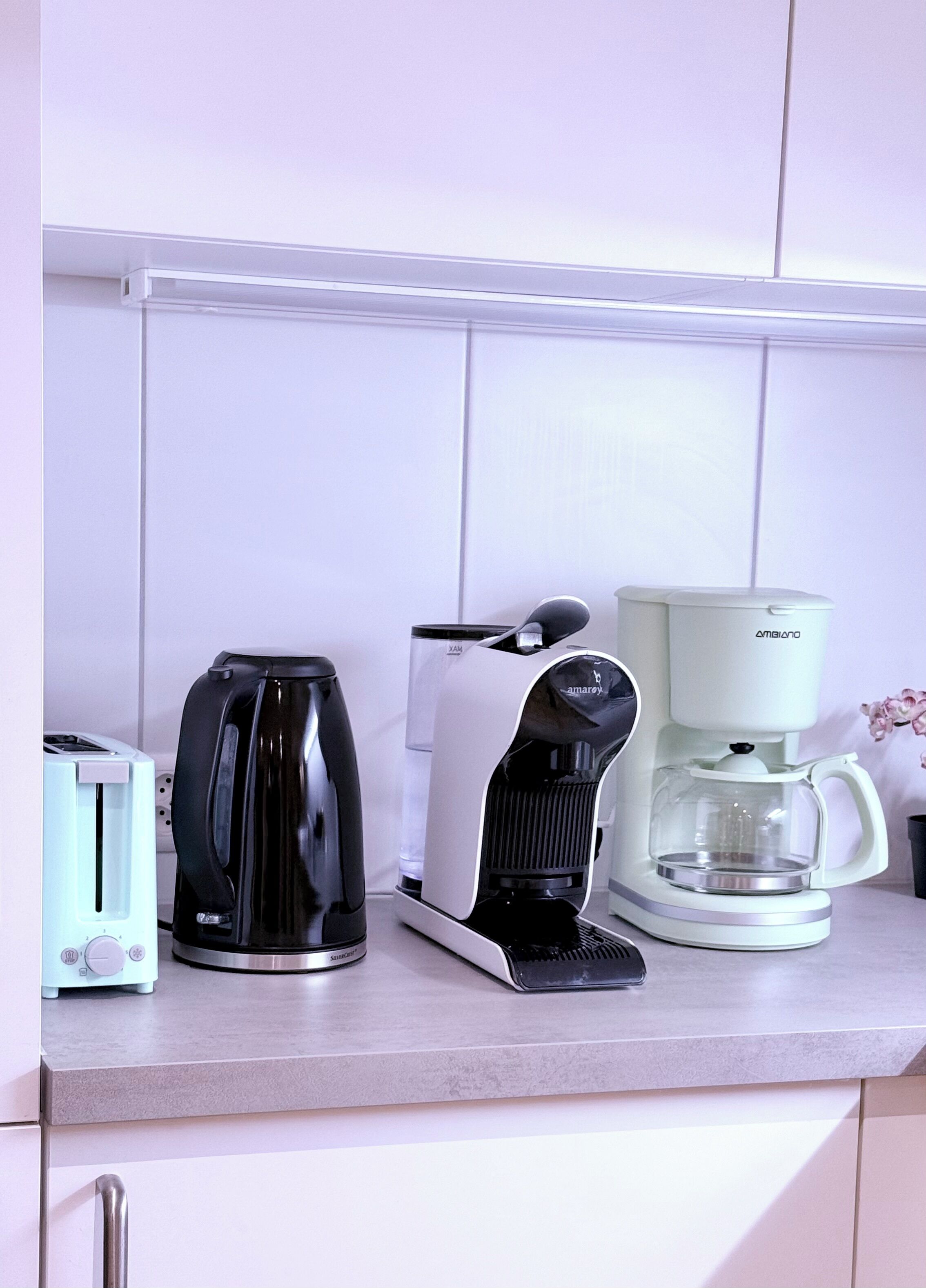 Uma bancada de cozinha com uma torradeira, uma cafeteira preta e branca e uma jarra de café branca.