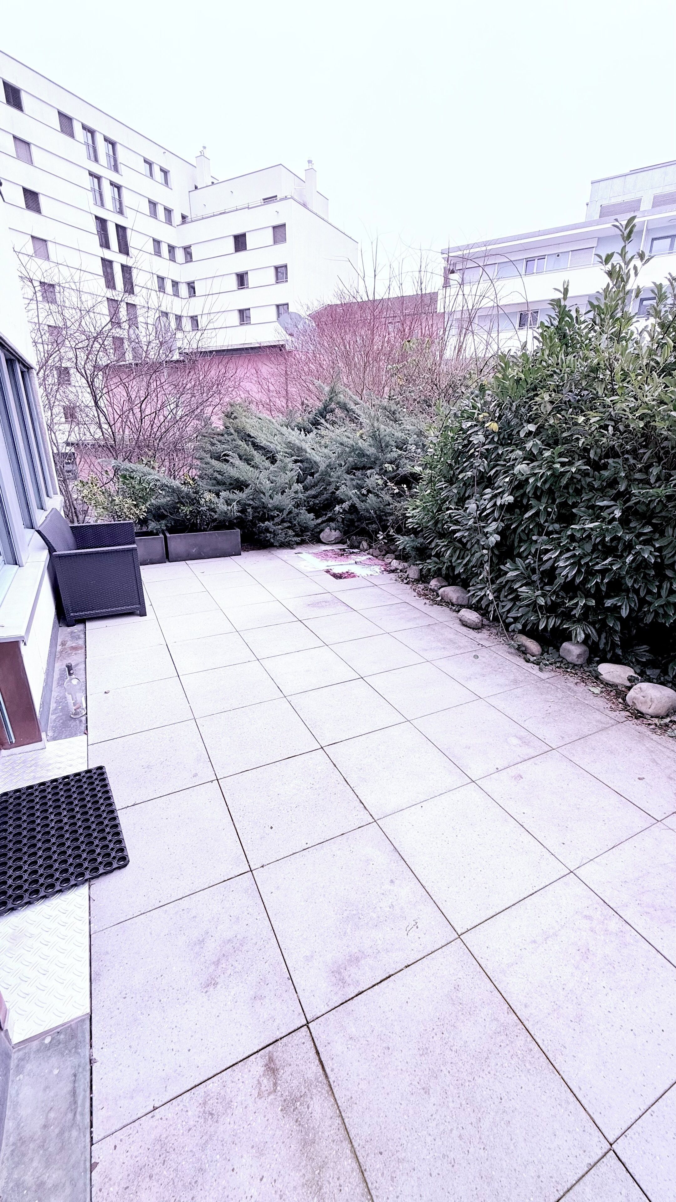 Eine Dachterrasse mit Fliesenboden, einer Sitzgelegenheit mit einem Stuhl und einer Reihe von Topfpflanzen.
