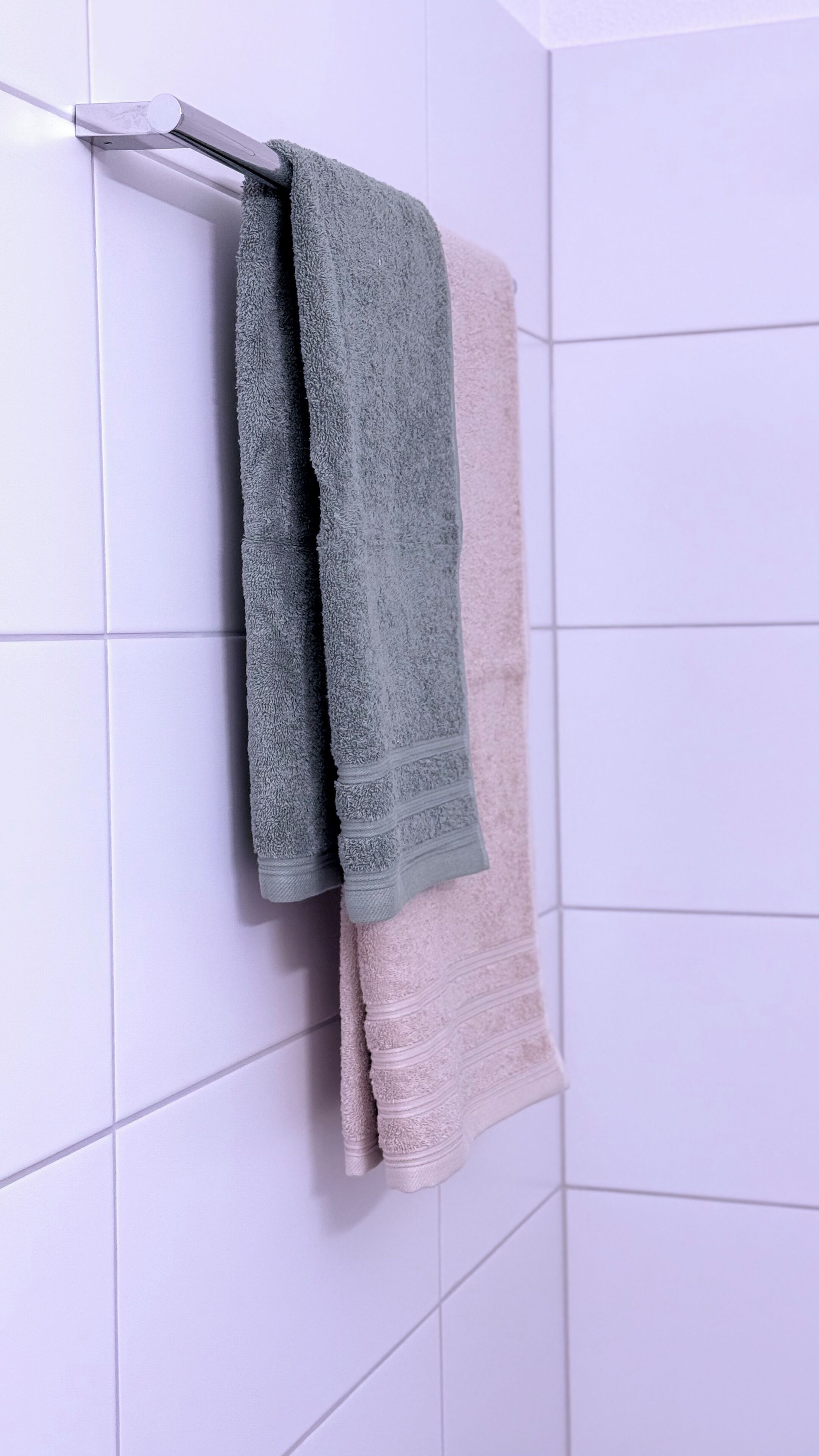 A bathroom with white tiled walls and a towel rack holding two towels.