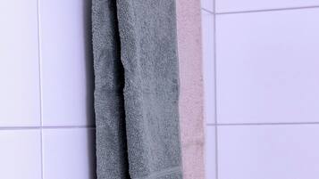 A bathroom with white tiled walls and a towel rack holding two towels.