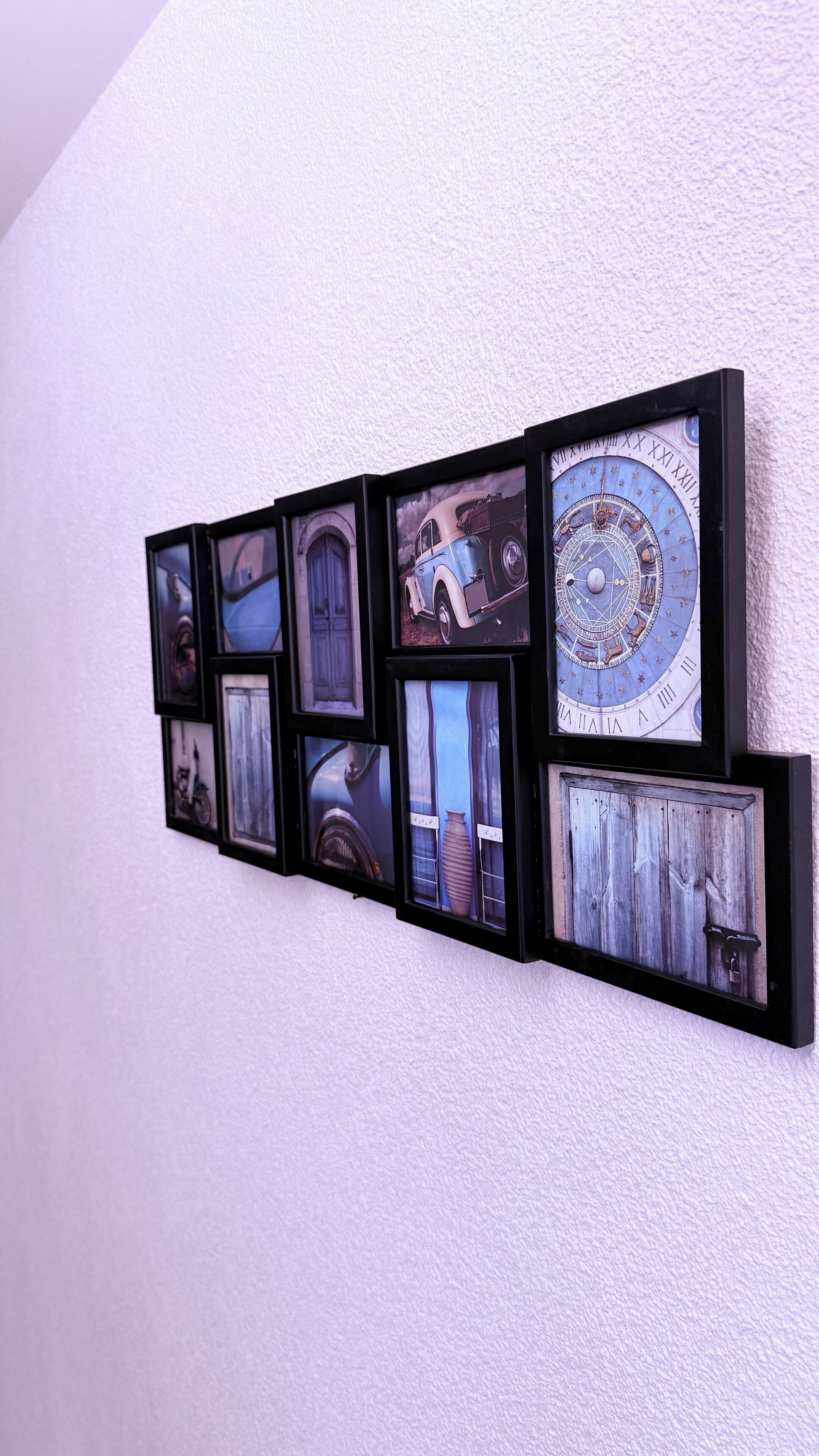 Una pantalla montada en la pared con varios cuadros enmarcados, incluyendo un coche antiguo, un reloj y elementos arquitectónicos.