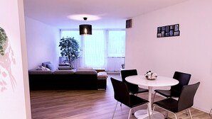 Een moderne woonkamer met een eethoek, houten vloeren, een bank, een eettafel met stoelen en een hanglamp.