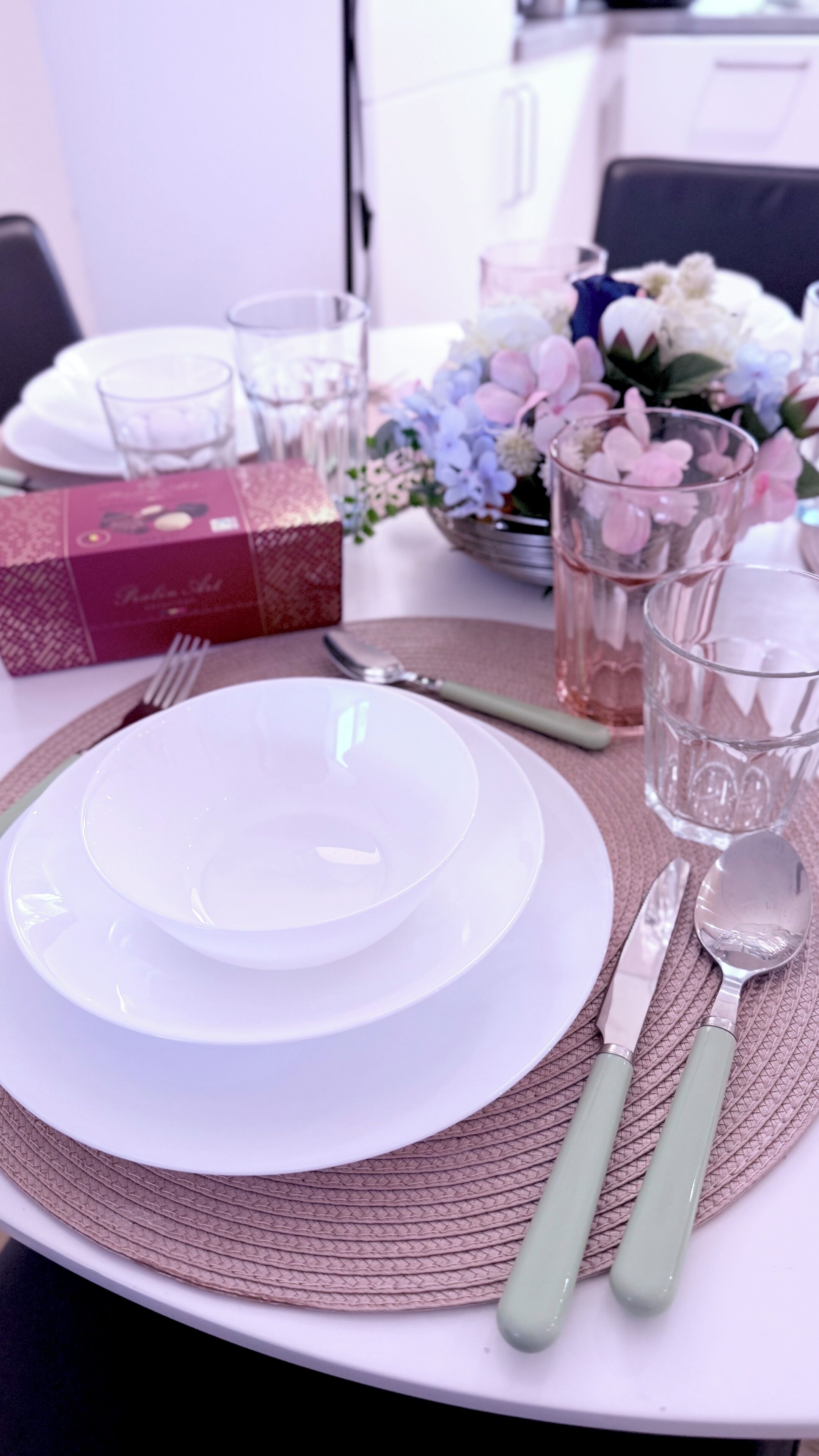 A table set with white plates, a red gift box, clear glasses, and a floral arrangement.