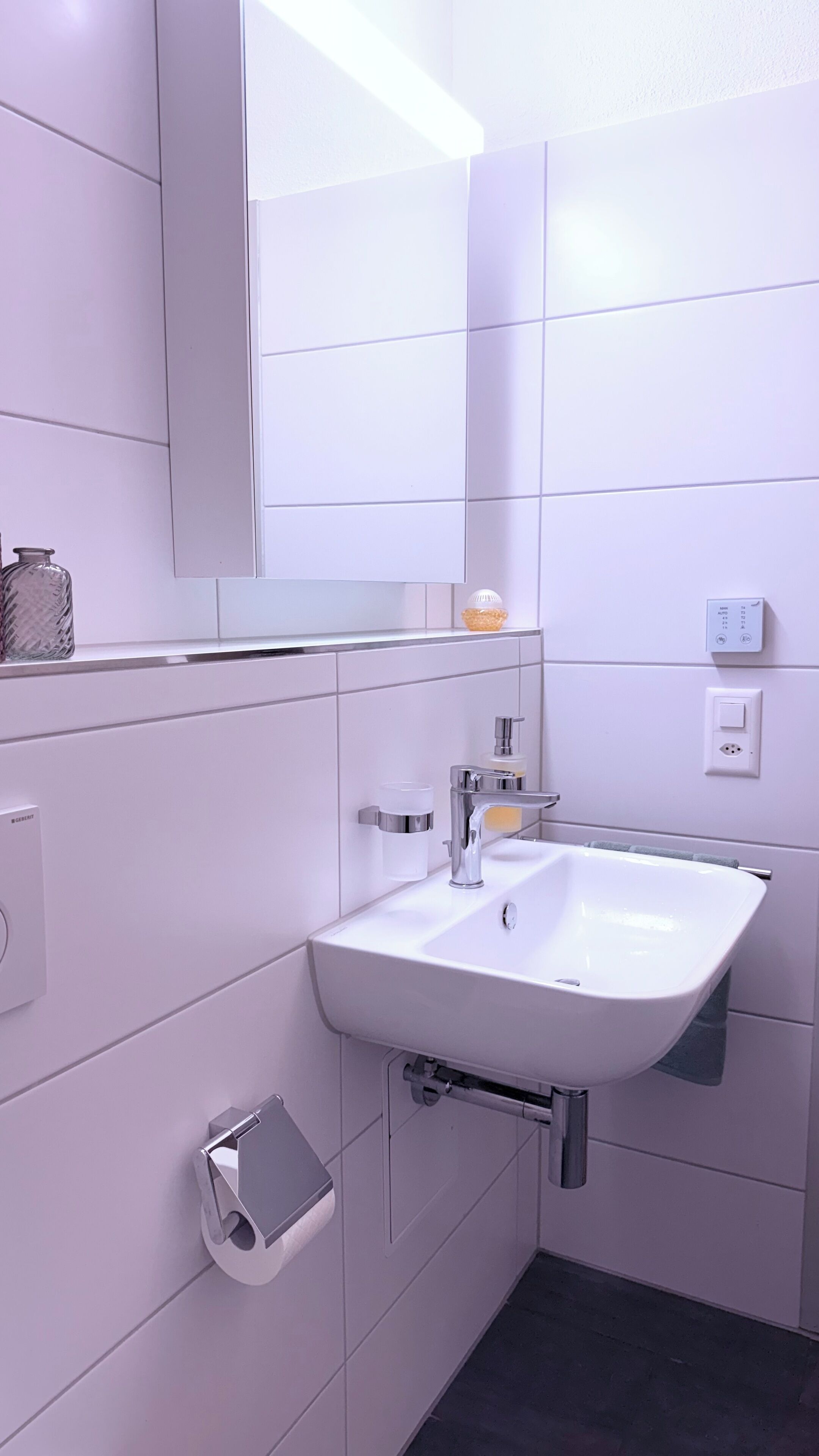 Een moderne badkamer met een witte wastafel, spiegel en betegelde wanden.