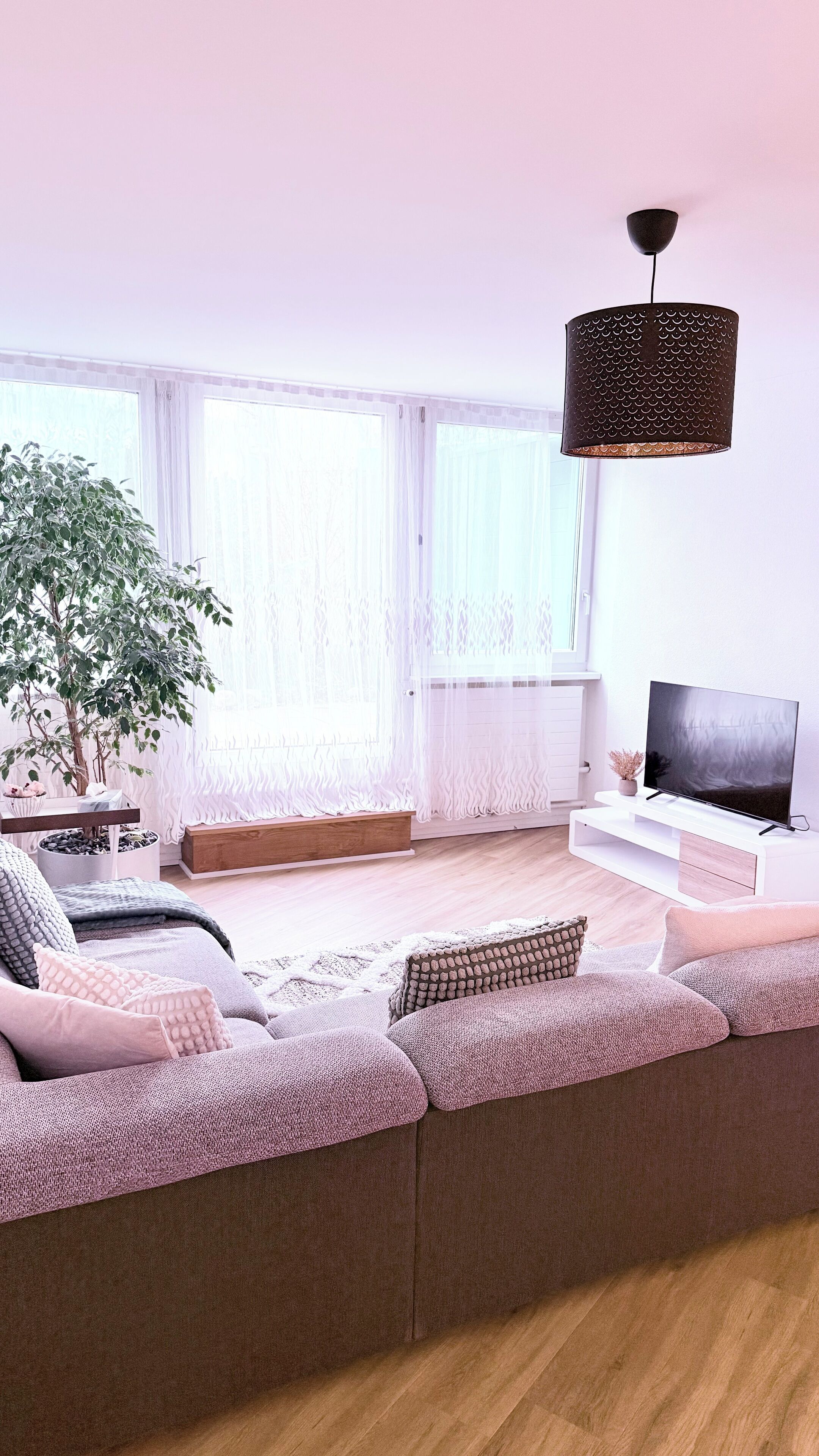 A modern living room with a large sofa, a television, and a hanging lamp.